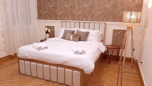 A neatly made bed with white linens and rolled towels, a wooden headboard, a bedside table with a lamp, and a herringbone-patterned wooden floor. - Royal Apartment in Talaat Harb Downtown  (Cairo)