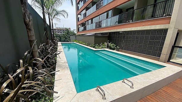 Uma piscina retangular com borda revestida em azulejo, rodeada por um deck de madeira e vegetação exuberante.