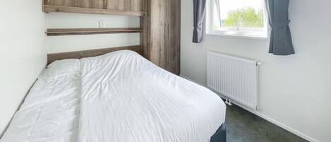 A bedroom with a bed, wooden headboard, window with curtains, and a radiator.