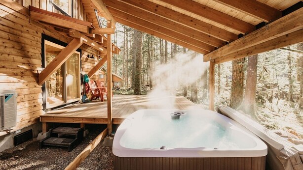 A wooden cabin with a hot tub on a deck, surrounded by trees. - 39gs - Hot Tub - Wi-fi - Pets Ok 3 Bedroom Cabin by RedAwning (Deming)