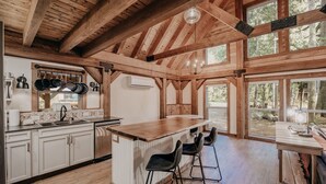 A spacious kitchen with wooden beams, a large island, and a view of the forest. - 39gs - Hot Tub - Wi-fi - Pets Ok 3 Bedroom Cabin by RedAwning (Deming)