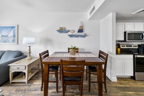 Ein Essbereich mit Holztisch und -stühlen, einem kleinen Topfpflanzen und einem an der Wand befestigten Regal mit Dekoration.