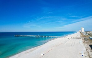Ein Strand mit einem Steg, der sich ins Meer erstreckt, einem sandigen Ufer und einigen Gebäuden im Hintergrund.