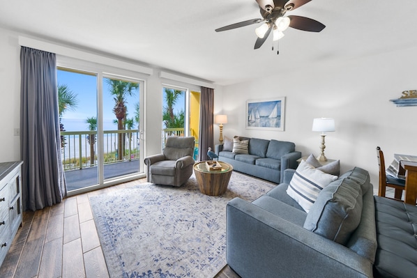 Ein geräumiges Wohnzimmer mit Balkon, Deckenventilator und einem Gemälde mit Segelbooten.