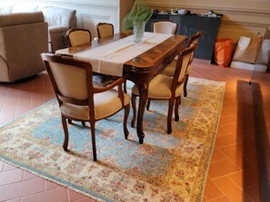 A dining area with a wooden table, four chairs, a floral rug, and a sofa in the background. - Stunning renovated Apartment with all amenities and a spacious terrace  (Cortona)