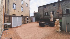 Un patio con mobiliario exterior, un edificio de piedra y una estatua.