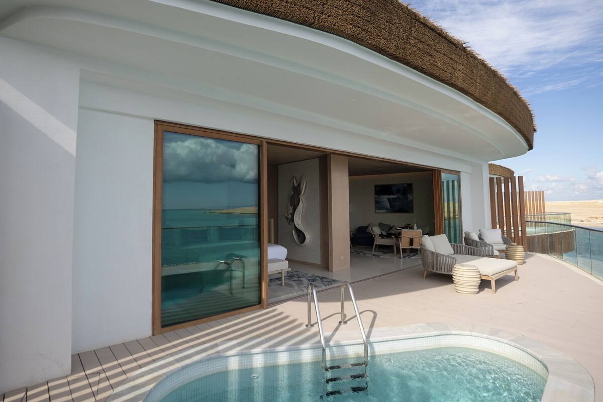 A modern outdoor pool area with a hot tub, lounge chairs, and a glass balustrade overlooking the sea.