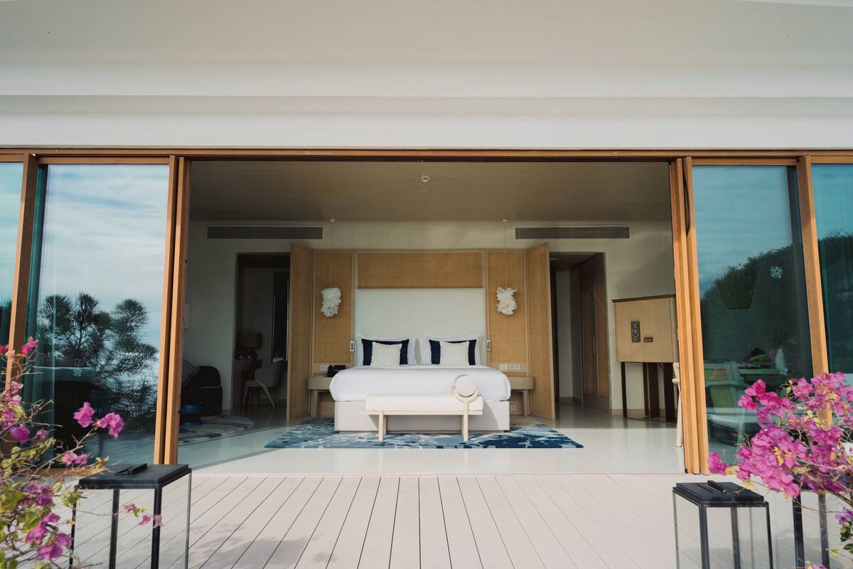 A modern bedroom with a large bed, sliding glass doors leading to a balcony, and a view of the outdoors.