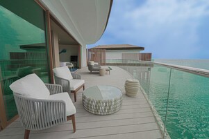 Una terraza con asientos al aire libre, una mesa de vidrio y vista al océano.