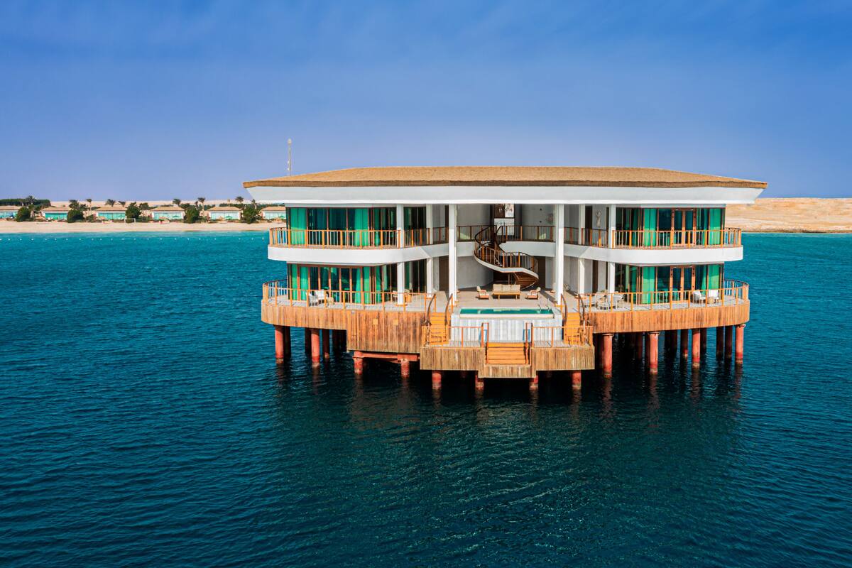 A multi-level waterfront building with a central staircase, outdoor seating, and a pool.
