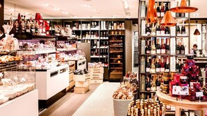 Una tienda bien iluminada con estantes llenos de diversos productos, entre ellos botellas y cajas, y una exposición de pasteles.