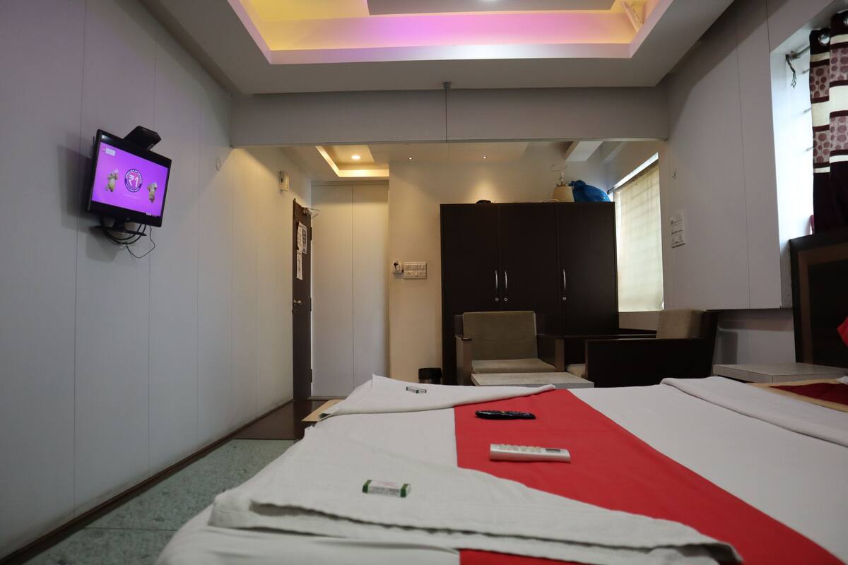 Quarto de hotel com cama, televisão na parede, guarda-roupa e secretária com cadeira.