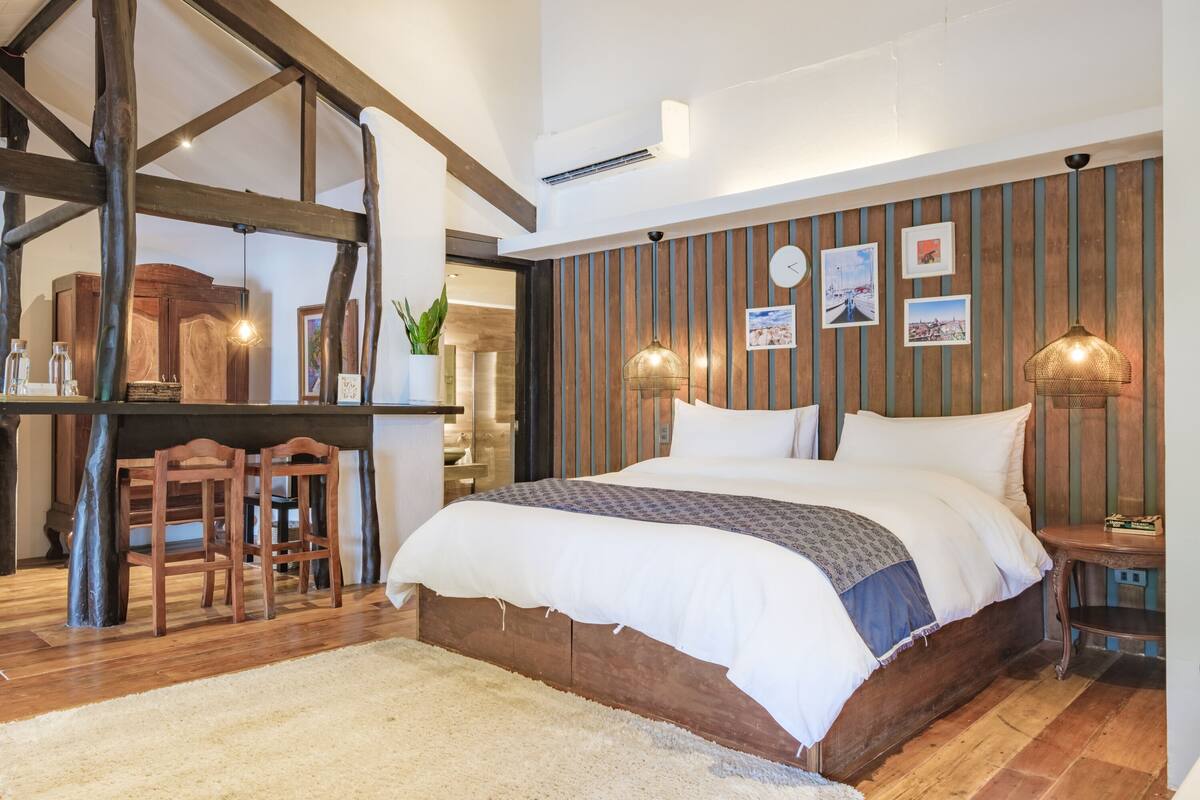A bedroom with a wooden bed, a desk with chairs, and a large window.