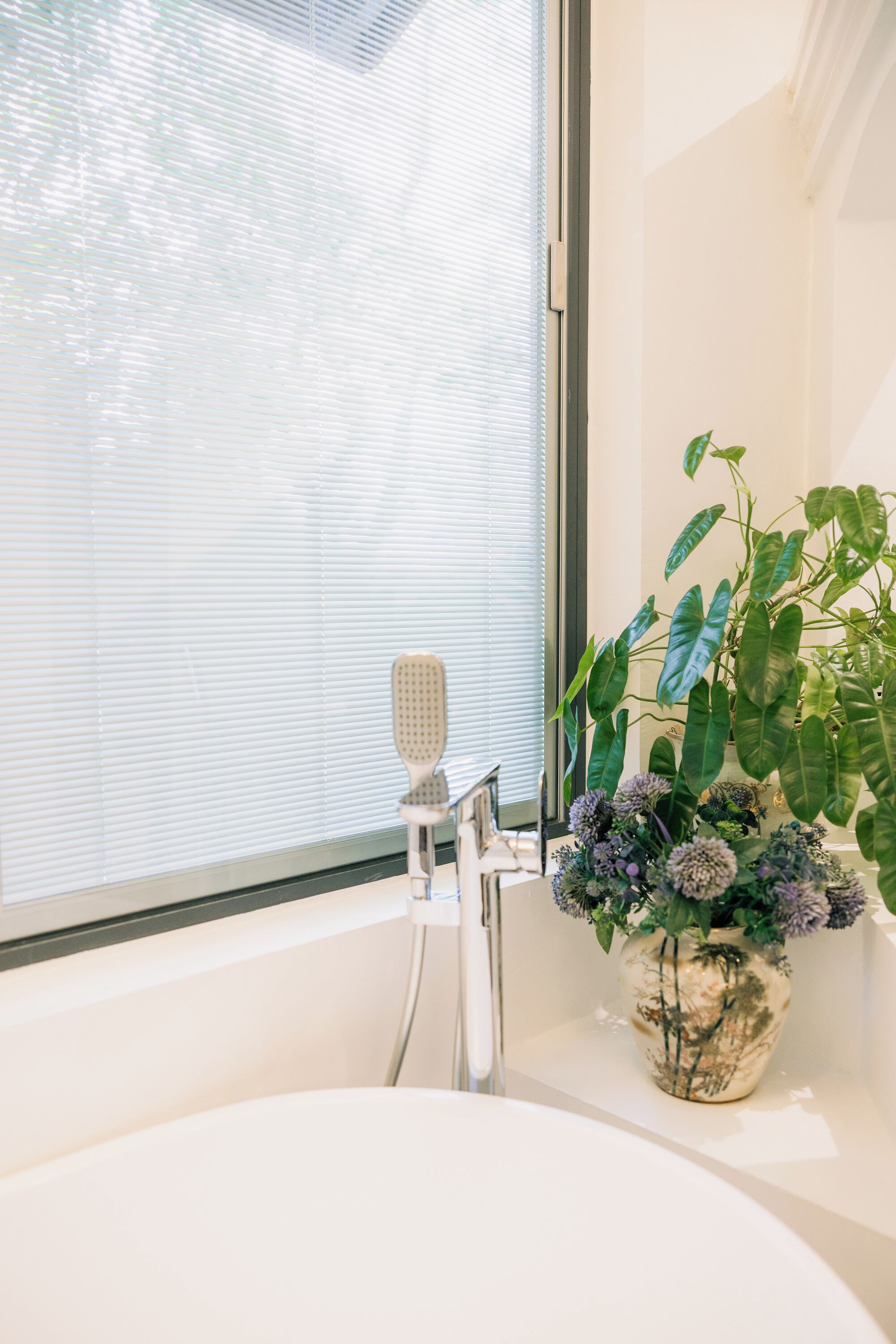 A bathroom with a bathtub, a shower, and a window with blinds.