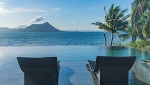 An infinity pool with two wicker chairs facing a view of the ocean and a mountain. - Nuuk Taal Lake (Laurel)