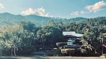 A waterfront property with a traditional building, lush greenery, and a view of distant hills.