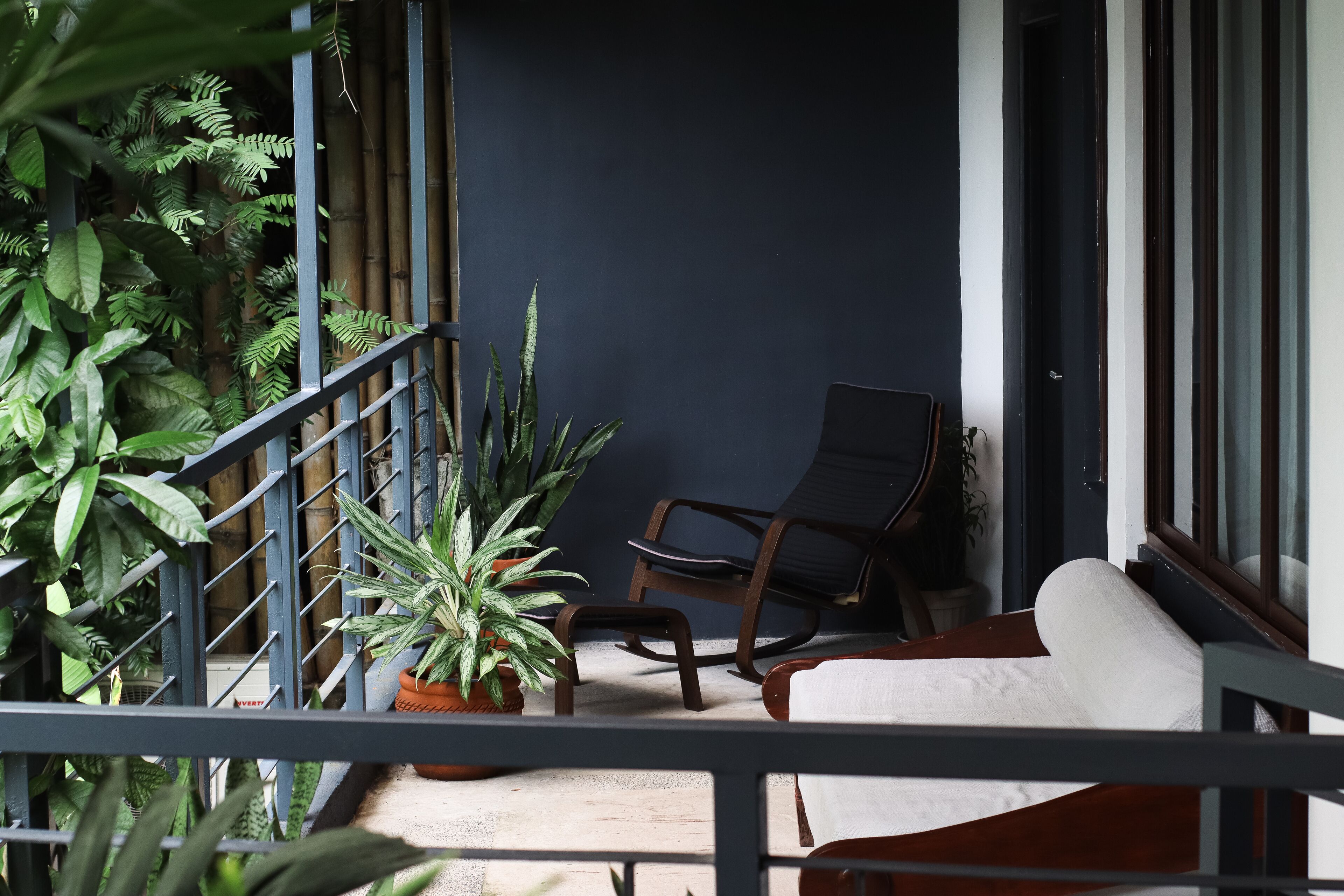 A balcony with a sofa, a chair, and potted plants.