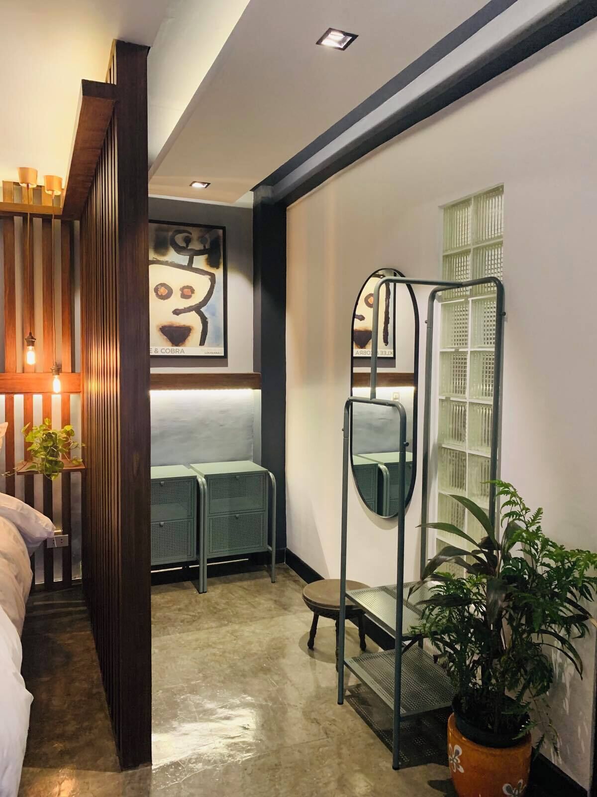 A modern room with a bed, a green sofa, a metal ladder, a potted plant, and a framed artwork on the wall.
