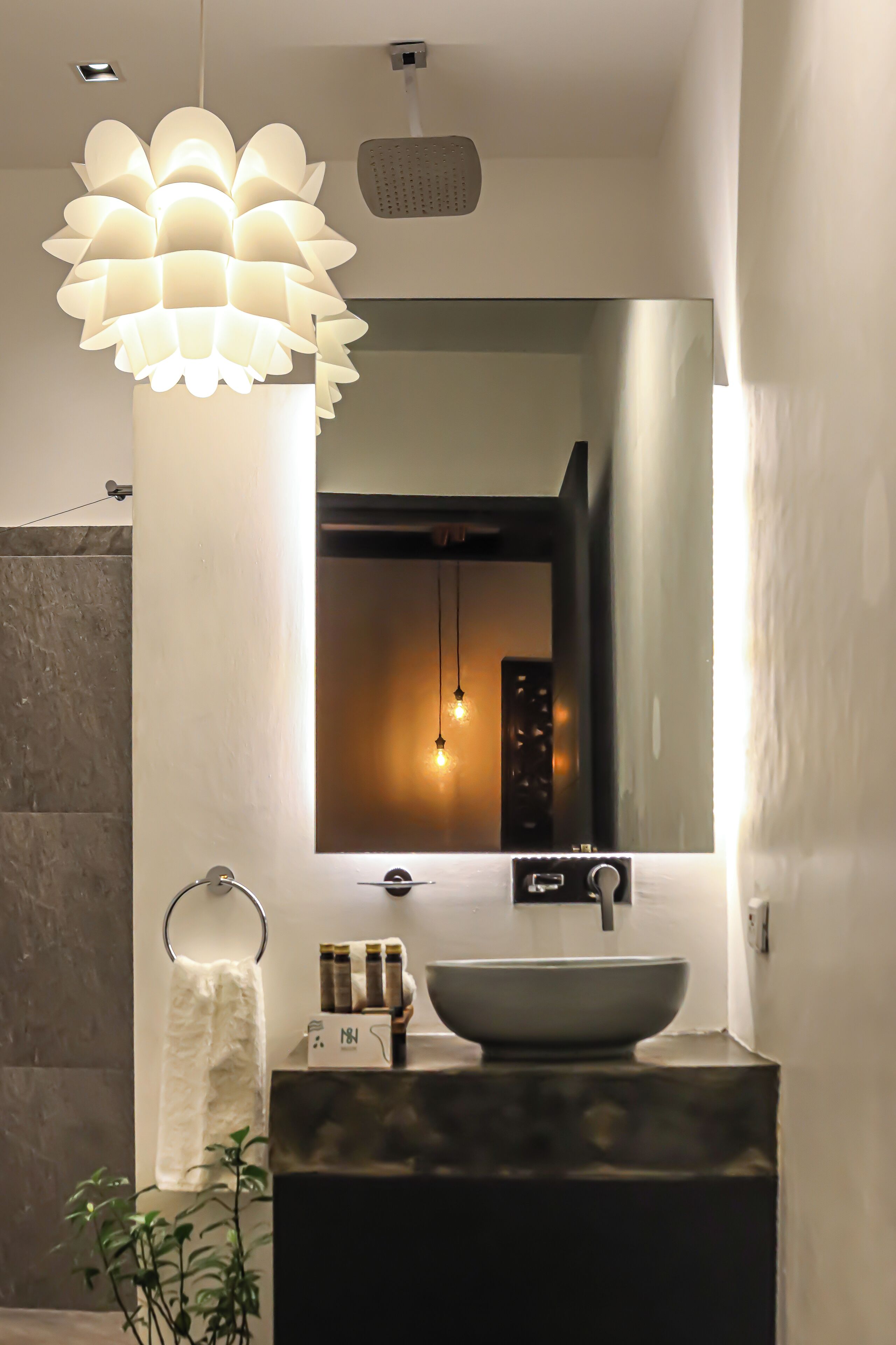 A modern bathroom with a large mirror, a vessel sink, and a unique light fixture.