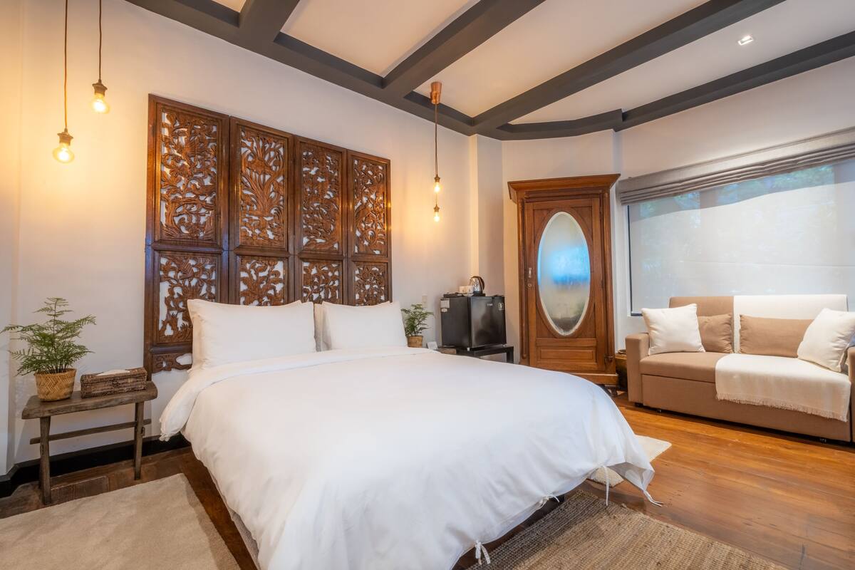 A bedroom with a large bed, a wooden headboard, a sofa, a TV, and a window with a view.