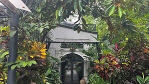 Un chemin menant à un bâtiment doté d’une entrée en arc de cercle, entouré d’une végétation tropicale luxuriante.