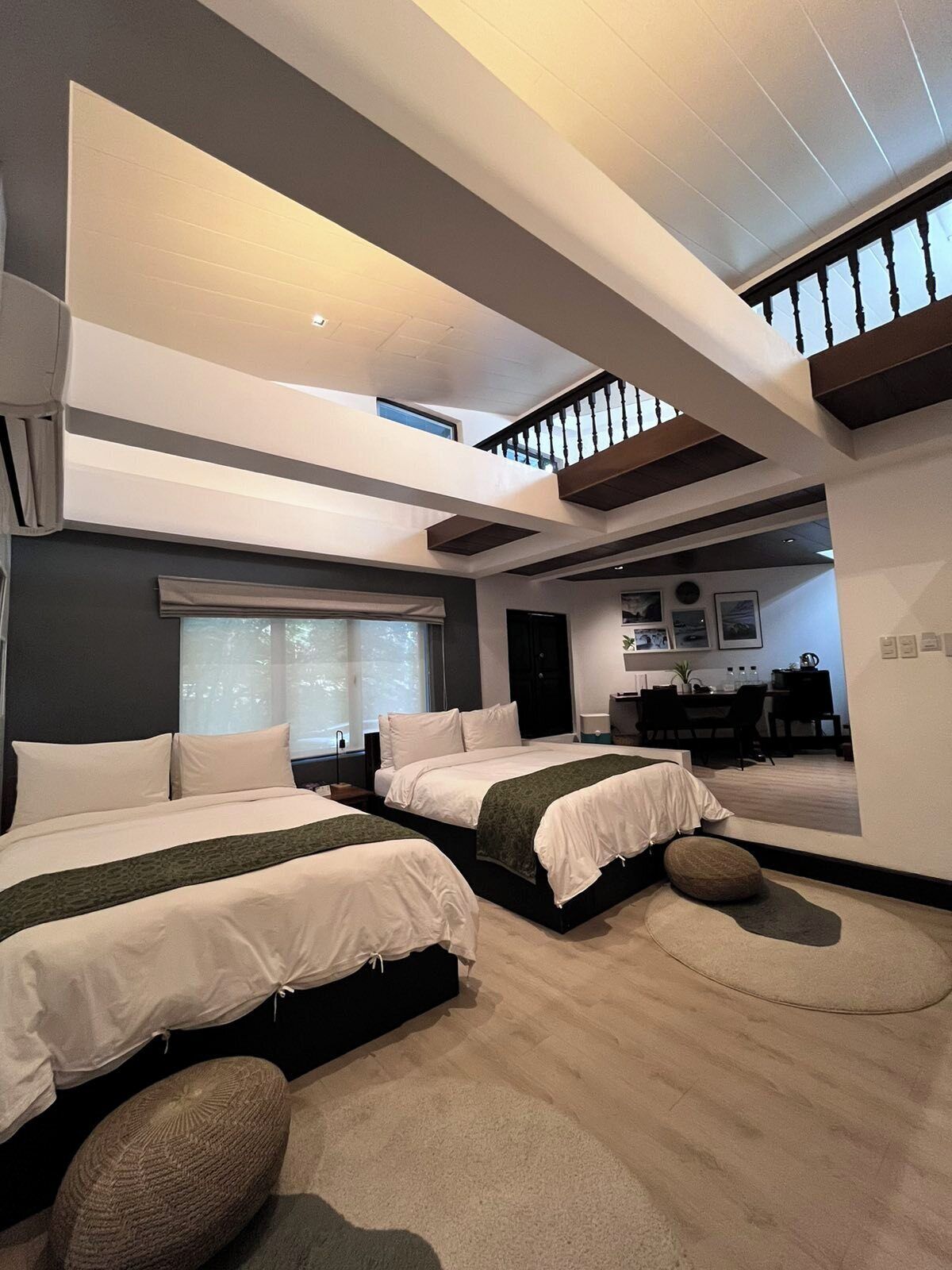 A modern bedroom with two beds, a skylight, and a dining area in the background.