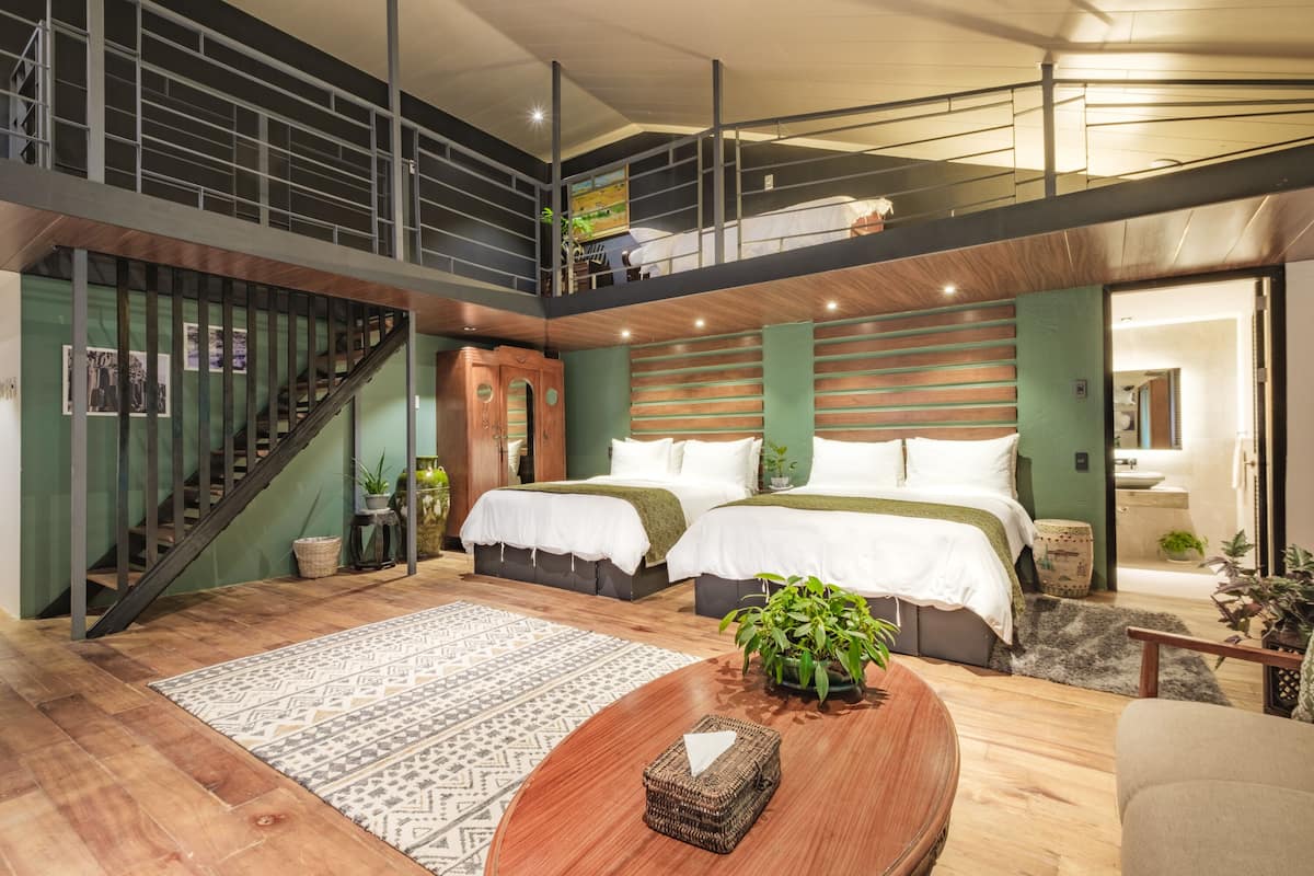 A modern hotel room with a loft-style design, featuring a large bed, a staircase, and a view of the city.