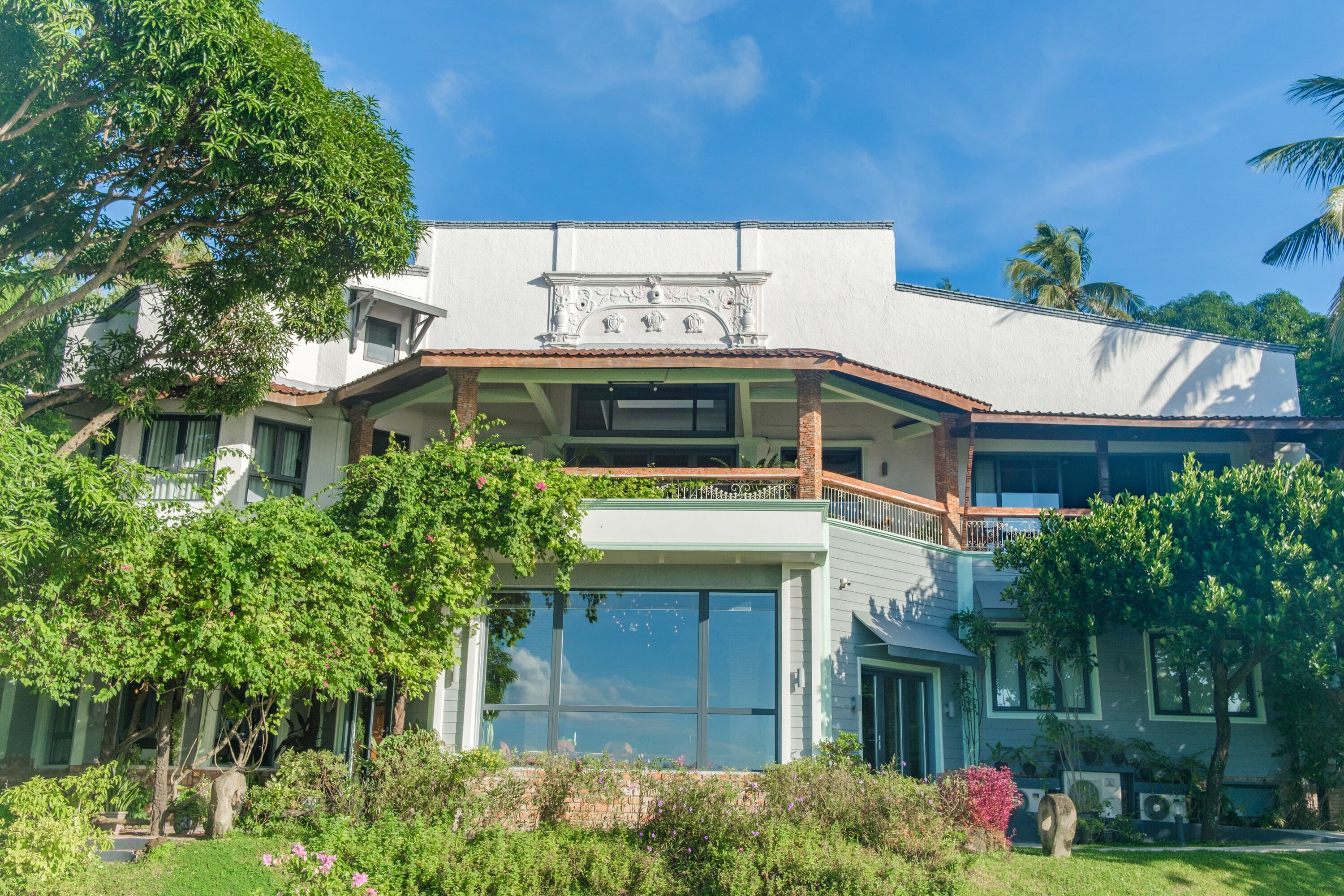 A two-story building with a balcony, large windows, and a garden area with various plants and flowers.