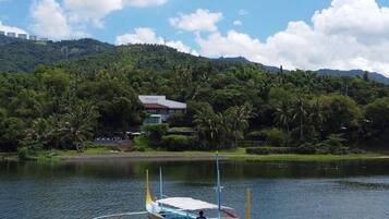 A traditional boat on a calm lake with a backdrop of lush greenery and a house on a hill.