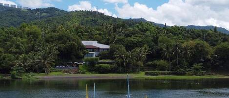 A traditional boat on a calm lake with a backdrop of lush greenery and a house on a hill.