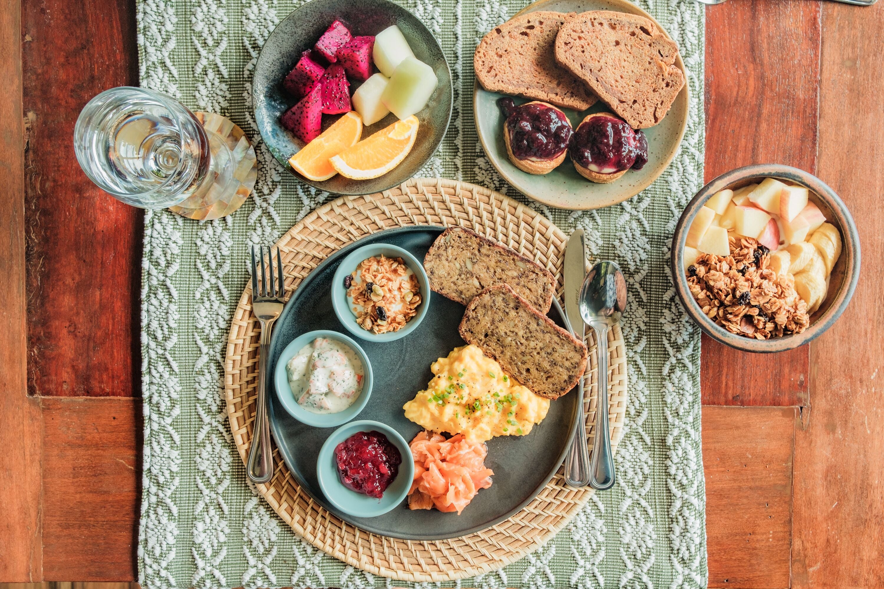 Disposição para o café da manhã com diversos alimentos em um descanso tecido, incluindo torradas, frutas e uma tigela de granola.