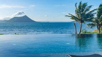 Relax by the infinity pool overlooking the ocean, surrounded by lush tropical scenery and palm trees.