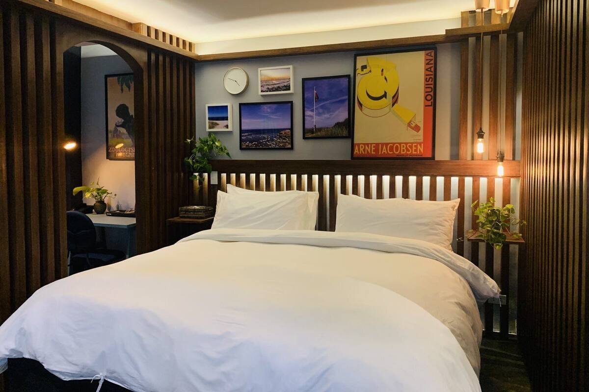 A bedroom with a large bed, wooden headboard, and a wall decorated with framed pictures and a clock.