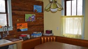 Un coin repas avec une table et des bancs en bois, une fenêtre avec des rideaux jaunes et des éléments de décoration murale, notamment un personnage de dessin animé et un panneau.