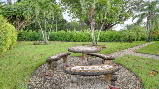 A garden with a stone table and benches surrounded by gravel, with trees and grass in the background. - Spacious + Serene Miami Home: Walk to Metrorail! (Miami)