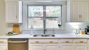 A kitchen with white cabinets, a double sink, a window, and a dish rack. - Centrally Located Home ~ Steps to Oxford Square! (Oxford)