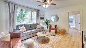 A living room with a sofa, armchairs, a coffee table, a ceiling fan, a large window, and a door leading to another room. - Centrally Located Home ~ Steps to Oxford Square! (Oxford)