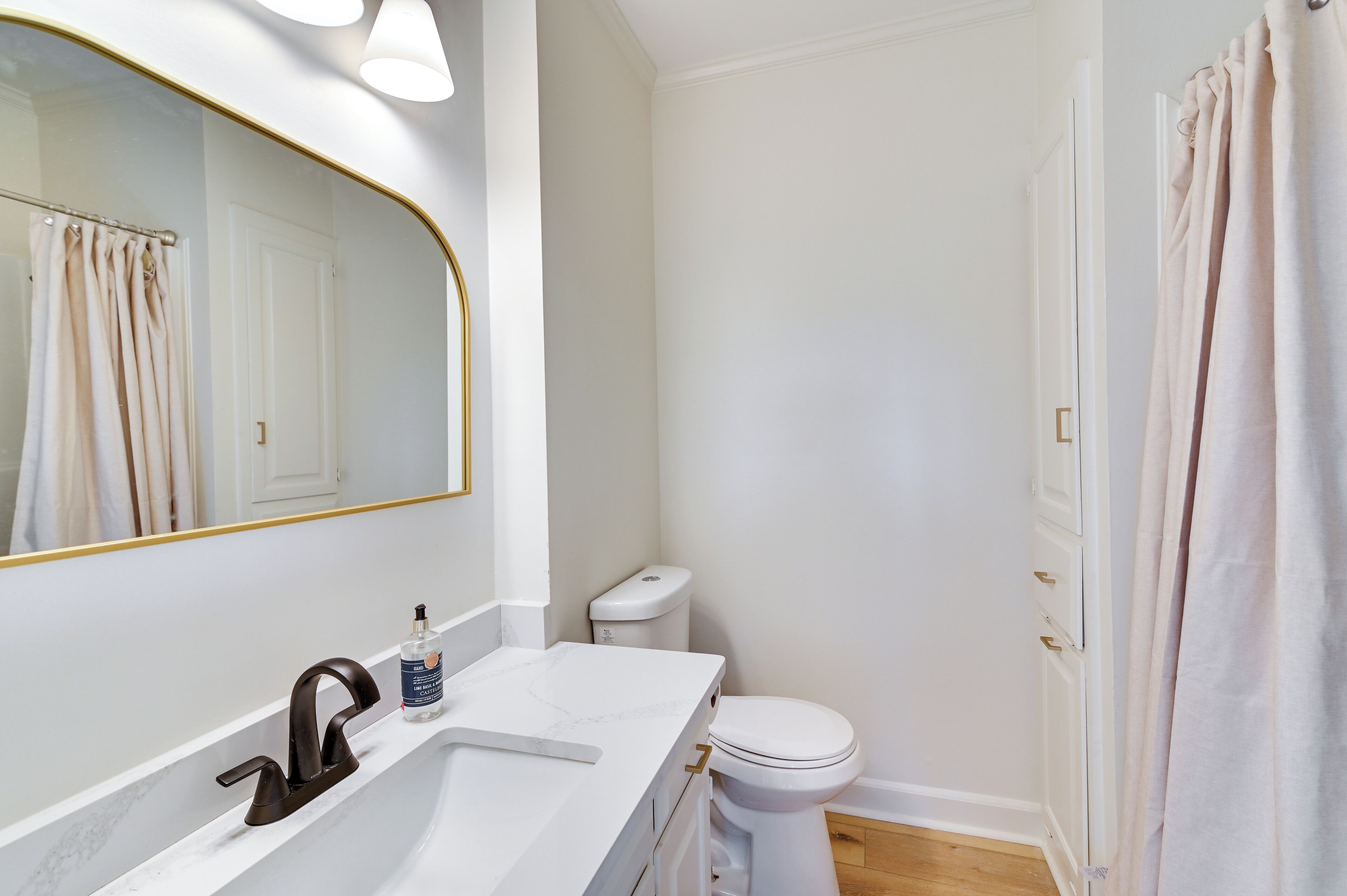 A bathroom with a white sink, a mirror with a gold frame, a toilet, and a shower curtain.