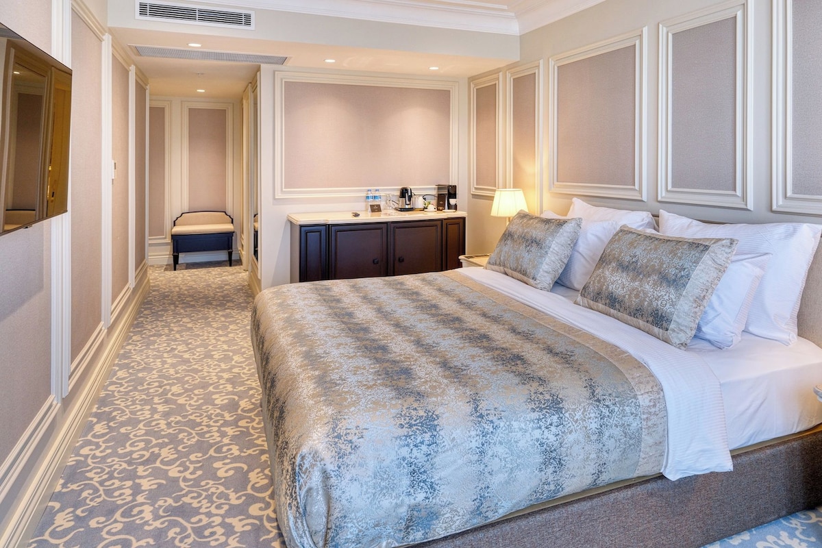 A hotel room with a large bed, a bedside table, a desk with a lamp, and a chair.
