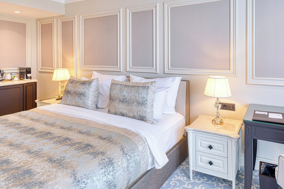 A hotel room with a bed, bedside tables, a desk, and a lamp.