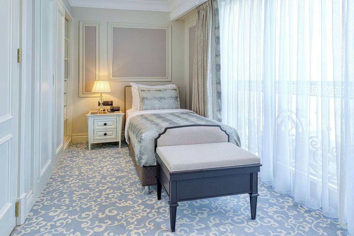 A hotel room with a bed, bedside table, lamp, and a bench.