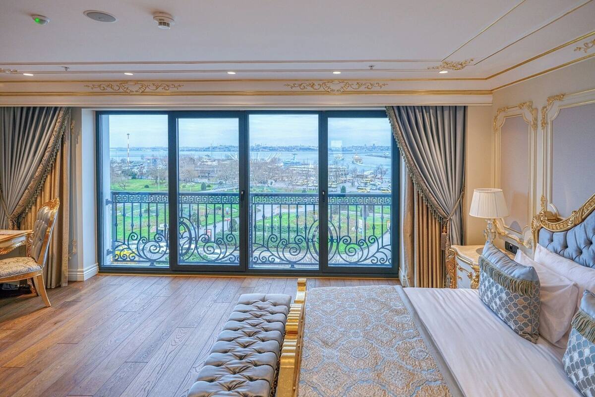 A spacious bedroom with a large bed, a bench, and a view of a cityscape through a balcony.