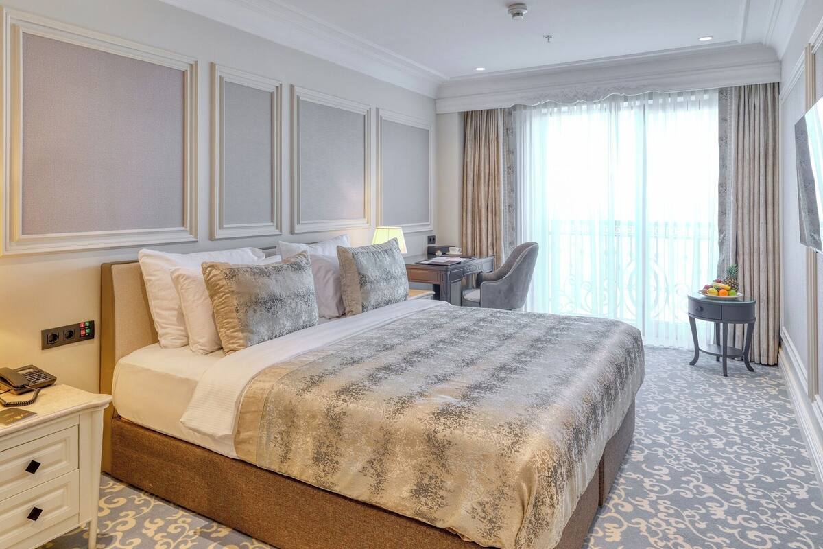 A hotel room with a large bed, bedside table with a lamp, a desk, and a chair.