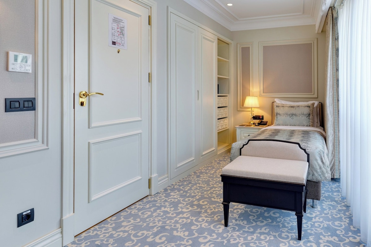 A hotel room with a bed, bedside table, lamp, and a small bench.