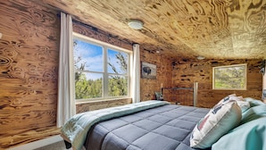 Une chambre dans une cabane en bois, avec un grand lit, deux fenêtres et un luminaire au plafond.