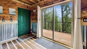 L’intérieur d’une cabane en bois, avec une porte verte, une porte-fenêtre coulissante donnant sur une terrasse et un extincteur.