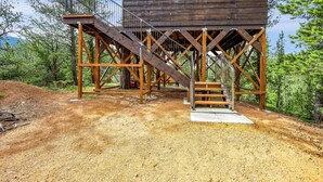 Une structure en bois avec un escalier menant à une plateforme, le tout entouré d’arbres.