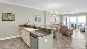 A spacious kitchen with a dishwasher, a dining area with a table and chairs, and a view of the ocean through large windows.