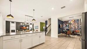 Une cuisine moderne dotée d’un grand îlot central, de luminaires suspendus et d’un coin repas agrémenté d’une fresque colorée.