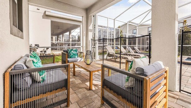 Une terrasse ensoleillée avec des sièges d’extérieur, une table en bois et une vue sur un jardin et une piscine.